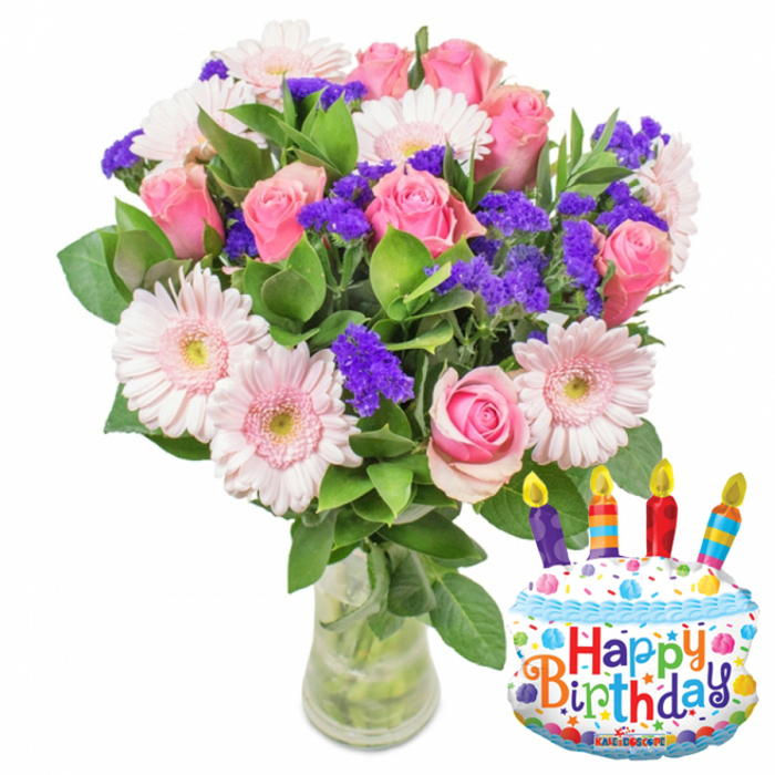 This image presents a festive floral gift arranged with careful balance: full, soft-pink roses form the heart of the display, petals layered and slightly ruffled as they catch the light, while pale pink Gerbera daisies radiate around them with broad, graceful petals and soft yellow centers that lift the palette. Interspersed among the larger blooms are clusters of bright purple filler-statice or limonium-whose small, papery textures create delightful points of contrast and visual rhythm. A few tiny white blossoms peek through, lending a delicate highlight among the pastels, and glossy, deep-green foliage frames the blooms, providing a lush, garden-fresh backdrop. The bouquet sits in a clear glass vase with a gently wider base, the stems and clear water visible below, communicating freshness and a clean presentation. To the right, a whimsical foil balloon shaped like a layered birthday cake enhances the celebratory tone: white frosted tiers bordered with blue icing, colorful sprinkles in red, yellow, green, and blue dotting the surface, and four striped candles-purple, red, orange, and blue-each topped with a small yellow flame. Playful, multi-coloured letters spell Happy Birthday across the front, and the small brand mark KALEIDOSCOPE sits near the bottom edge of the balloon. The overall impression is tender and joyful, an arrangement that would suit sending warm birthday wishes around Camberwell, from Brunswick Park to Camberwell Road, with the soft scent of roses lingering like a fond memory.