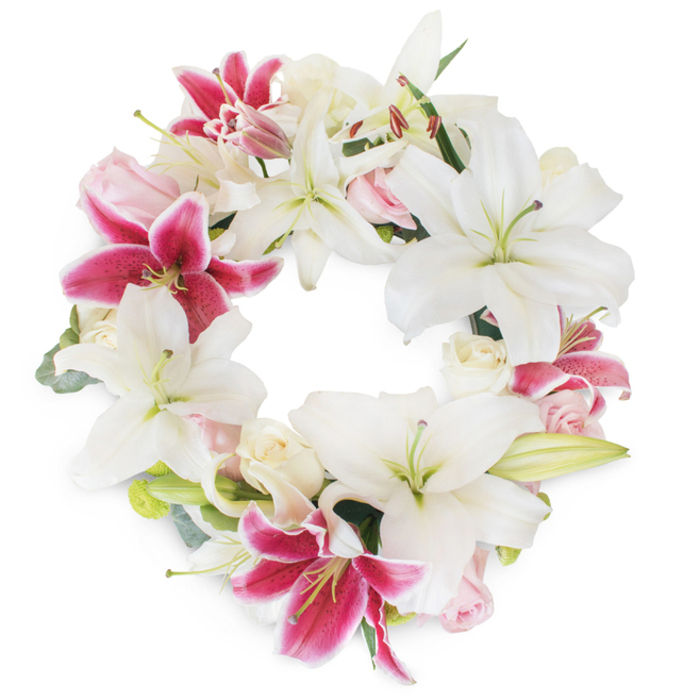 A radiant floral tribute assembled by Camberwell's dedicated team, this sumptuous wreath is composed of luxuriant white lilies and vibrant fuchsia Stargazer lilies, each bloom artfully arranged to form a complete circle full of both serenity and vibrancy. The white Oriental lilies-majestic in size and luminous in hue-anchor the design, their open petals revealing slender, pale green and yellow stamens. Breathing life and colour between the whites, the Stargazer lilies shimmer with fuchsia and magenta, their petals marked by delicate speckles and radiant undertones. The circle is completed by soft nests of blush pink and creamy white roses, some tightly closed, others unfurling in gentle blooms, their petals buttery and plush-a reminder of life's tender moments. Threaded among the florals, fresh eucalyptus and muted green foliage weave subtle texture and structure, reminiscent of the calming greenery found in Myatt's Fields Park. This wreath evokes a profound sense of completeness and unity, its carefully balanced palette both dignified and uplifting. Designed for cherished commemorations, funerals, or to accompany a message of sympathy, it stands as a testament to Camberwell Flowers' local expertise and sensitivity, available for delivery throughout SE5. Each petal and leaf contributes to a solemn yet hopeful arrangement, celebrating memory and conveying heartfelt remembrance in the local Camberwell community.