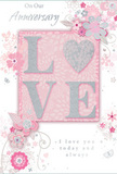 This anniversary card presents a refined celebration of enduring romance, using a harmony of soft pastel pinks, pearly whites, and muted silvery greys that recall the gentle tones of an early morning in Camberwell. At the centre, the word LOVE is rendered in softly raised glitter, its surface smooth yet textured enough for fingertips to feel each letter. The O is replaced by a shimmering silver heart, subtly embossed so it catches the light like a small piece of jewellery, becoming the emotional core of the design. Around this focal word, delicate blossoms in blush and mauve unfurl with a watercolour softness, their edges diffused as though lightly brushed by hand. Slender stems and curling tendrils sway across the card, forming arcs and loops that give the layout a sense of gentle motion, like flowers turning toward the light in a sheltered Camberwell garden. Tiny details-floating petals, graceful swirls and understated butterflies-add an element of playfulness while maintaining a sophisticated feel. The background is a calm, powdery pink, allowing the silvery highlights and floral outlines to stand out without overwhelming the eyes. Above and below the central motif, in a refined, flowing script, appear the words On Our Anniversary and I love you today and always, set in a tone that feels quietly sincere rather than overly ornate. The whole card gives the impression of a hand-tied bouquet translated into paper, reminiscent of the soft, romantic designs often prepared for couples across SE5 and collected on the way home from Camberwell Flowers to mark another year shared together.
